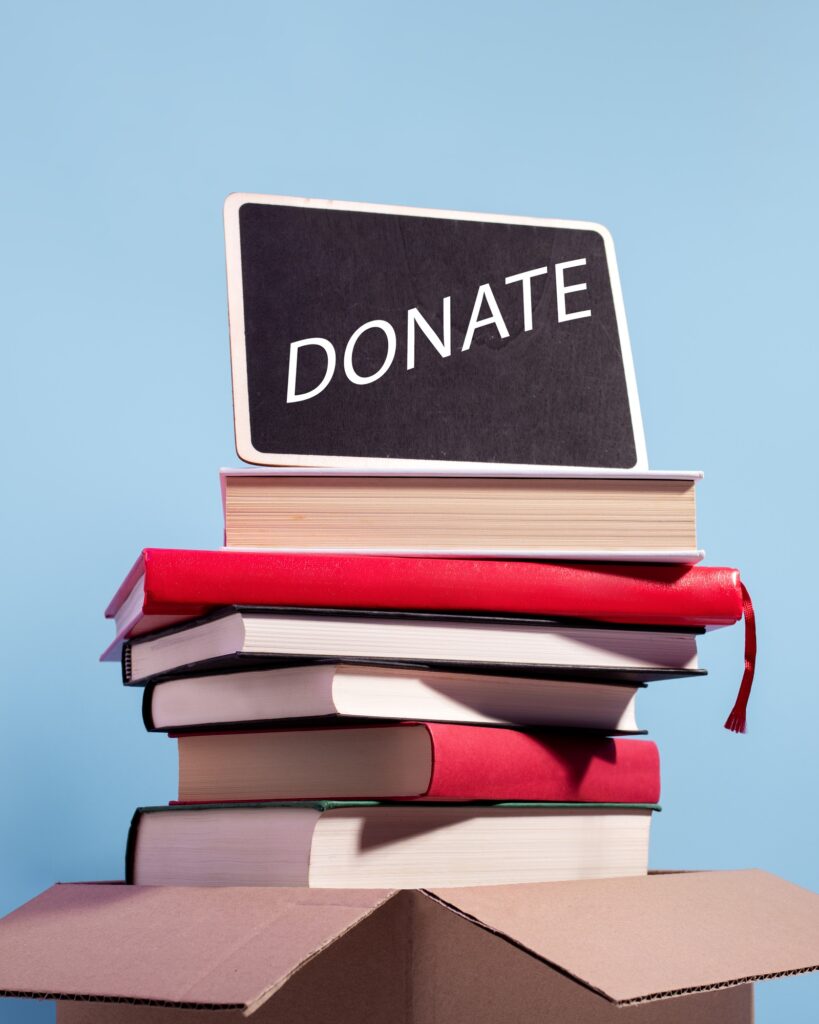 Books in a box ready for donation on blue with Donation sign for text, copy space.